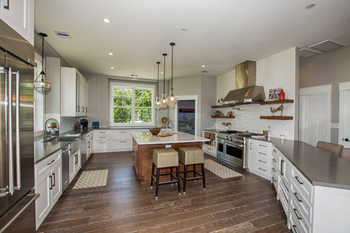 Large transitional u-shaped medium tone wood floor and multicolored floor open concept kitchen photo in Houston with a farmhouse sink, shaker cabinets, white cabinets, quartz countertops, white backsplash, subway tile backsplash, stainless steel appliances and an island