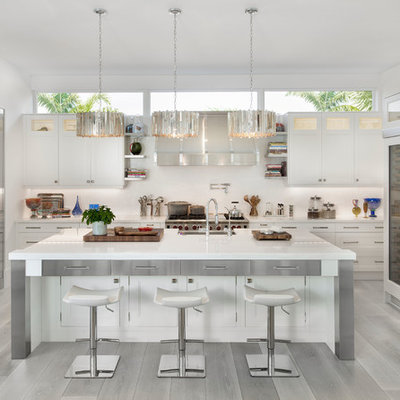 Example of a beach style u-shaped light wood floor and gray floor kitchen design in Miami with a farmhouse sink, white cabinets, white backsplash, stainless steel appliances, an island and shaker cabinets