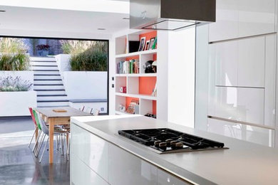 Design ideas for a medium sized modern galley kitchen/diner in Los Angeles with a double-bowl sink, flat-panel cabinets, white cabinets, composite countertops, red splashback, brick splashback, integrated appliances, concrete flooring, an island, grey floors and white worktops.