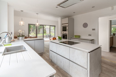 Inspiration for a medium sized contemporary l-shaped open plan kitchen in Buckinghamshire with a double-bowl sink, flat-panel cabinets, white cabinets, engineered stone countertops, white appliances, vinyl flooring, an island, beige floors and white worktops.