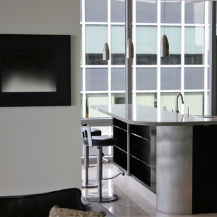Diseño de cocina en L, moderna, grande, abierta, con una isla, fregadero bajoencimera, armarios con paneles lisos, puertas de armario negras, encimera de acrílico, salpicadero de piedra caliza, electrodomésticos de acero inoxidable, suelo de piedra caliza y suelo beige