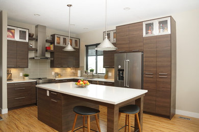 Example of a trendy l-shaped medium tone wood floor and brown floor kitchen design in Salt Lake City with an undermount sink, flat-panel cabinets, medium tone wood cabinets, beige backsplash, subway tile backsplash, stainless steel appliances, an island and white countertops