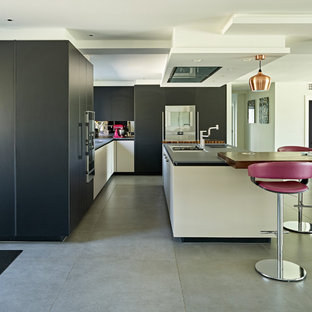 This is an example of a large contemporary l-shaped open plan kitchen in Hertfordshire with flat-panel cabinets, black cabinets, concrete flooring, an island, grey floors and black worktops.