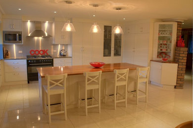 Exempel på ett stort lantligt kök, med en undermonterad diskho, skåp i shakerstil, vita skåp, träbänkskiva, stänkskydd med metallisk yta, glaspanel som stänkskydd, svarta vitvaror, klinkergolv i terrakotta och en köksö
