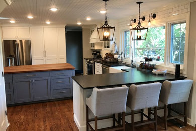 Inspiration for a large rural u-shaped enclosed kitchen in Other with a belfast sink, shaker cabinets, white cabinets, composite countertops, white splashback, metro tiled splashback, stainless steel appliances, dark hardwood flooring, an island and brown floors.
