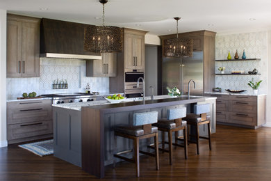 Large island style l-shaped medium tone wood floor and brown floor open concept kitchen photo in Denver with an undermount sink, recessed-panel cabinets, gray cabinets, white backsplash, marble backsplash, stainless steel appliances, an island, white countertops and marble countertops