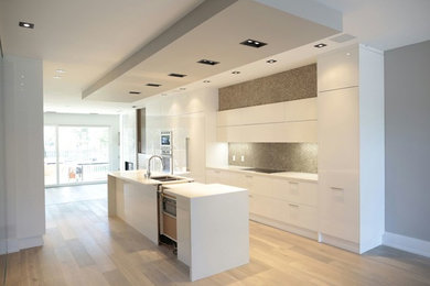 This is an example of a medium sized contemporary single-wall kitchen in Toronto with a double-bowl sink, flat-panel cabinets, white cabinets, quartz worktops, grey splashback, ceramic splashback, integrated appliances, light hardwood flooring and an island.
