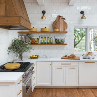 Inspiration pour une cuisine ouverte minimaliste en L avec un évier de ferme, des portes de placard blanches, une crédence blanche, une crédence en carreau de céramique, un électroménager en acier inoxydable, un sol en bois brun, un plan de travail en quartz, un îlot central et un placard à porte shaker.