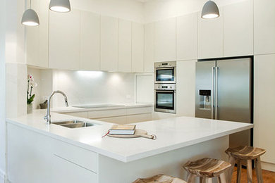 Inspiration för ett funkis kök, med en undermonterad diskho, vitt stänkskydd, släta luckor, vita skåp, marmorbänkskiva, stänkskydd i marmor, rostfria vitvaror, mellanmörkt trägolv och en halv köksö