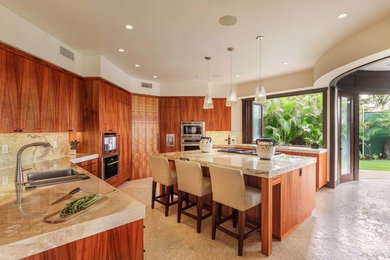 ハワイにある高級な広いコンテンポラリースタイルのおしゃれなアイランドキッチン (フラットパネル扉のキャビネット、中間色木目調キャビネット、御影石カウンター、シルバーの調理設備) の写真