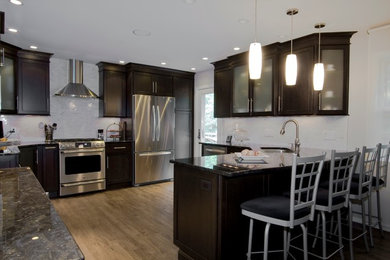 Modern inredning av ett mellanstort kök, med en undermonterad diskho, granitbänkskiva, vitt stänkskydd, stänkskydd i keramik, rostfria vitvaror, skåp i shakerstil, svarta skåp, mörkt trägolv, en halv köksö och brunt golv