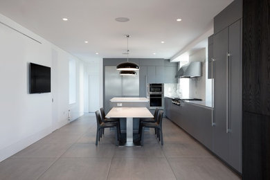 Large contemporary l-shaped kitchen/diner in London with a built-in sink, flat-panel cabinets, grey cabinets, engineered stone countertops, white splashback, stone slab splashback, stainless steel appliances, ceramic flooring, an island, grey floors and white worktops.