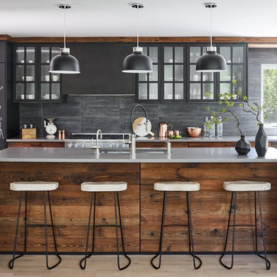 Inspiration for a mid-sized contemporary galley light wood floor and gray floor open concept kitchen remodel in New York with concrete countertops, stone tile backsplash, paneled appliances, an island, gray countertops, an undermount sink, medium tone wood cabinets, gray backsplash and glass-front cabinets