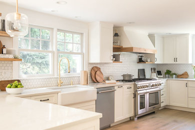 Eat-in kitchen - large farmhouse u-shaped light wood floor and brown floor eat-in kitchen idea in Boston with a farmhouse sink, shaker cabinets, white cabinets, quartz countertops, white backsplash, mosaic tile backsplash, stainless steel appliances, a peninsula and white countertops