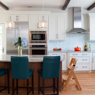 Exemple d'une grand cuisine américaine parallèle moderne avec un îlot central, un placard à porte shaker, des portes de placard blanches, une crédence en carreau de verre, un électroménager en acier inoxydable, un plan de travail en granite, un sol marron, un sol en bois brun, un évier de ferme et une crédence bleue.