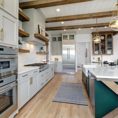 Open concept kitchen - large country l-shaped light wood floor and beige floor open concept kitchen idea in Boise with a farmhouse sink, shaker cabinets, white cabinets, quartz countertops, white backsplash, subway tile backsplash, stainless steel appliances, an island and white countertops