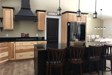 Country l-shaped open concept kitchen photo in Other with a farmhouse sink, flat-panel cabinets, light wood cabinets, granite countertops, an island and black countertops