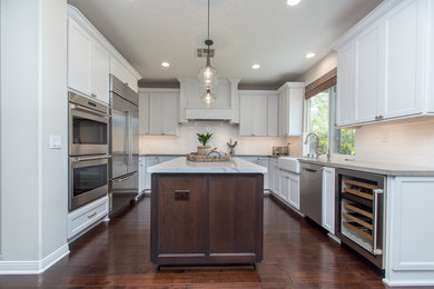 Example of a mid-sized cottage u-shaped dark wood floor and brown floor kitchen pantry design in Orange County with a farmhouse sink, shaker cabinets, white cabinets, quartz countertops, white backsplash, subway tile backsplash, stainless steel appliances and an island