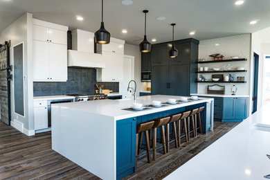 Example of a huge urban u-shaped medium tone wood floor and brown floor eat-in kitchen design in Edmonton with a farmhouse sink, shaker cabinets, blue cabinets, quartz countertops, multicolored backsplash, metal backsplash, stainless steel appliances and two islands