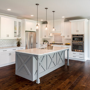 Design ideas for a country l-shaped eat-in kitchen in Philadelphia with a double-bowl sink, shaker cabinets, white cabinets, white splashback, subway tile splashback, stainless steel appliances, dark hardwood floors, with island and brown floor.