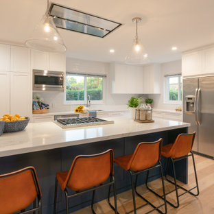 Photo of a mid-sized midcentury l-shaped eat-in kitchen in Santa Barbara with an undermount sink, shaker cabinets, white cabinets, quartz benchtops, white splashback, subway tile splashback, stainless steel appliances, vinyl floors, with island, brown floor and white benchtop.