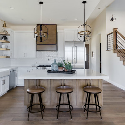 Example of a farmhouse l-shaped light wood floor kitchen design in Salt Lake City with a farmhouse sink, shaker cabinets, white cabinets, white backsplash, subway tile backsplash, stainless steel appliances, an island, white countertops and quartzite countertops