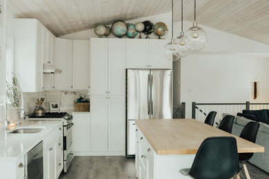 Example of a mid-sized danish l-shaped vinyl floor eat-in kitchen design in Vancouver with an undermount sink, shaker cabinets, white cabinets, quartz countertops, white backsplash, subway tile backsplash, stainless steel appliances and an island