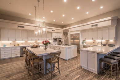 Inspiration for a huge transitional l-shaped dark wood floor and brown floor eat-in kitchen remodel in Phoenix with an undermount sink, recessed-panel cabinets, white cabinets, solid surface countertops, beige backsplash, ceramic backsplash, stainless steel appliances and a peninsula