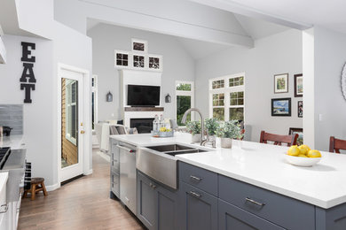 Large farmhouse light wood floor and beige floor eat-in kitchen photo in Seattle with a farmhouse sink, shaker cabinets, white cabinets, gray backsplash, subway tile backsplash, stainless steel appliances, an island and white countertops