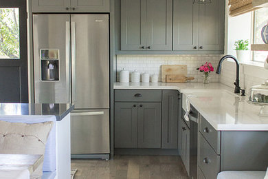 Inspiration for a large country medium tone wood floor eat-in kitchen remodel in Tampa with a farmhouse sink, shaker cabinets, gray cabinets, quartz countertops, white backsplash, subway tile backsplash, stainless steel appliances and an island