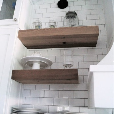 Example of a mid-sized cottage galley light wood floor and yellow floor open concept kitchen design in Other with a farmhouse sink, shaker cabinets, white cabinets, solid surface countertops, white backsplash, subway tile backsplash, stainless steel appliances, an island and black countertops