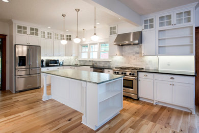 Example of a mid-sized farmhouse l-shaped light wood floor and brown floor eat-in kitchen design in Portland with a farmhouse sink, shaker cabinets, white cabinets, granite countertops, multicolored backsplash, marble backsplash, stainless steel appliances, an island and green countertops