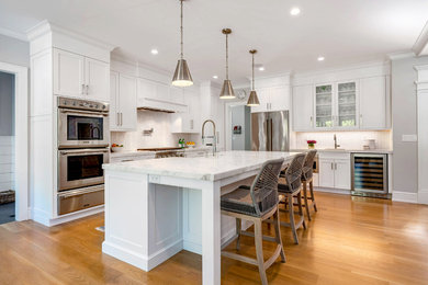 Inspiration for a large country l-shaped medium tone wood floor and brown floor eat-in kitchen remodel in Bridgeport with a farmhouse sink, recessed-panel cabinets, white cabinets, marble countertops, white backsplash, ceramic backsplash, stainless steel appliances, an island and white countertops