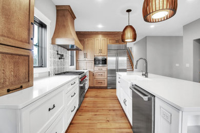 Country light wood floor and brown floor kitchen photo in New York with a farmhouse sink, white cabinets, white backsplash, ceramic backsplash, stainless steel appliances, an island and white countertops