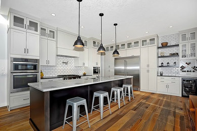 Large cottage l-shaped medium tone wood floor eat-in kitchen photo in Calgary with a farmhouse sink, shaker cabinets, granite countertops, white backsplash, ceramic backsplash, stainless steel appliances and an island