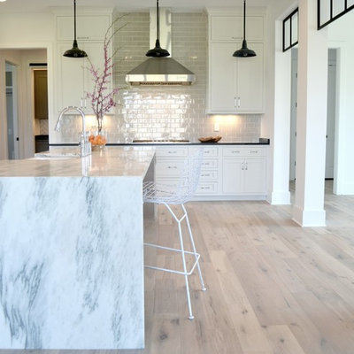 Inspiration for a large cottage l-shaped medium tone wood floor and beige floor kitchen remodel in Indianapolis with recessed-panel cabinets, white cabinets, marble countertops, gray backsplash, subway tile backsplash, stainless steel appliances, an island, a farmhouse sink and white countertops