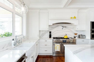 Eat-in kitchen - large traditional l-shaped medium tone wood floor and brown floor eat-in kitchen idea in Other with raised-panel cabinets, white cabinets, quartz countertops, white backsplash, stone slab backsplash, stainless steel appliances, an island, white countertops and a farmhouse sink