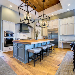 Large country l-shaped open plan kitchen in Austin with a farmhouse sink, shaker cabinets, grey cabinets, wood benchtops, white splashback, subway tile splashback, stainless steel appliances, medium hardwood floors, with island and beige floor.