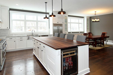Inspiration for a large modern l-shaped medium tone wood floor eat-in kitchen remodel in Minneapolis with a farmhouse sink, beaded inset cabinets, white cabinets, wood countertops, white backsplash, subway tile backsplash and stainless steel appliances
