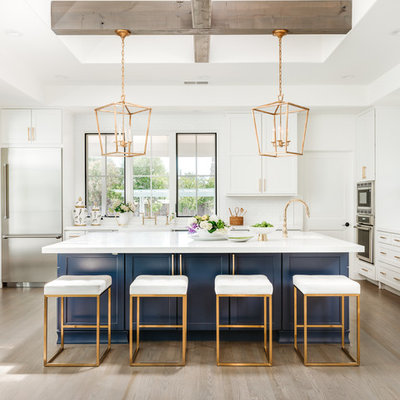 Inspiration for a large cottage l-shaped light wood floor and gray floor kitchen remodel in San Francisco with shaker cabinets, blue cabinets, white backsplash, an island, white countertops, a farmhouse sink, quartz countertops, ceramic backsplash and stainless steel appliances