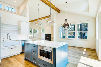 Mid-sized country l-shaped light wood floor eat-in kitchen photo in Portland with a farmhouse sink, shaker cabinets, white cabinets, solid surface countertops, white backsplash, subway tile backsplash, stainless steel appliances and an island