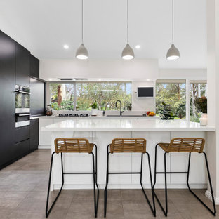 Photo of a large contemporary l-shaped kitchen pantry in Melbourne with a double-bowl sink, white cabinets, quartz benchtops, black appliances, terra-cotta floors and with island.