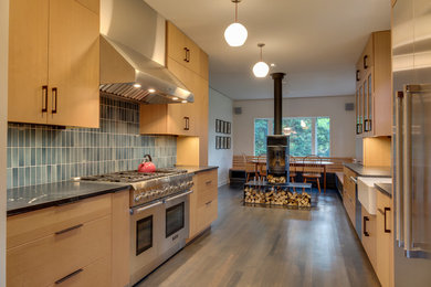 Example of a mid-sized minimalist galley medium tone wood floor eat-in kitchen design in Other with a farmhouse sink, flat-panel cabinets, light wood cabinets, quartzite countertops, blue backsplash, glass tile backsplash, stainless steel appliances and no island