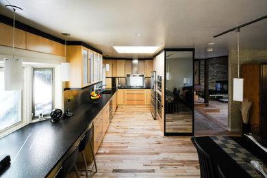 Imagen de cocina actual de tamaño medio con armarios con paneles lisos, puertas de armario de madera clara, electrodomésticos de acero inoxidable y suelo de madera clara