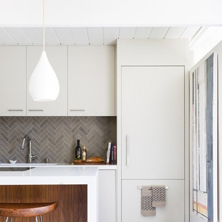 This is an example of a midcentury single-wall kitchen in San Francisco with an integrated sink, flat-panel cabinets, white cabinets, grey splashback, ceramic splashback, white appliances, concrete floors, with island and quartz benchtops.