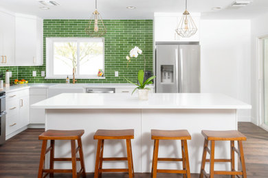 Inspiration for a mid-sized mid-century modern l-shaped vinyl floor and brown floor open concept kitchen remodel in Phoenix with a farmhouse sink, flat-panel cabinets, white cabinets, quartz countertops, green backsplash, ceramic backsplash, stainless steel appliances, an island and white countertops