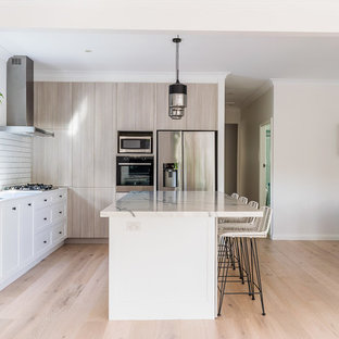 Mid-sized contemporary l-shaped open plan kitchen in Sydney with a double-bowl sink, quartz benchtops, white splashback, subway tile splashback, black appliances, light hardwood floors, with island, flat-panel cabinets, beige cabinets, beige floor and white benchtop.