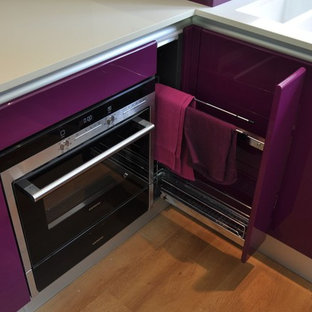 Cette photo montre une cuisine ouverte tendance en U de taille moyenne avec un évier posé, un placard à porte plane, des portes de placard violettes, un plan de travail en quartz, une crédence en feuille de verre, un électroménager noir, un sol en bois clair, une péninsule, un sol marron et un plan de travail blanc.