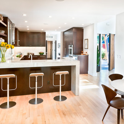 Eat-in kitchen - large contemporary u-shaped light wood floor eat-in kitchen idea in Los Angeles with flat-panel cabinets, dark wood cabinets, an undermount sink, quartz countertops, white backsplash, glass tile backsplash, stainless steel appliances and a peninsula