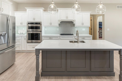 Mid-sized transitional l-shaped vinyl floor and brown floor eat-in kitchen photo in St Louis with an undermount sink, shaker cabinets, white cabinets, quartz countertops, gray backsplash, subway tile backsplash, stainless steel appliances, an island and white countertops